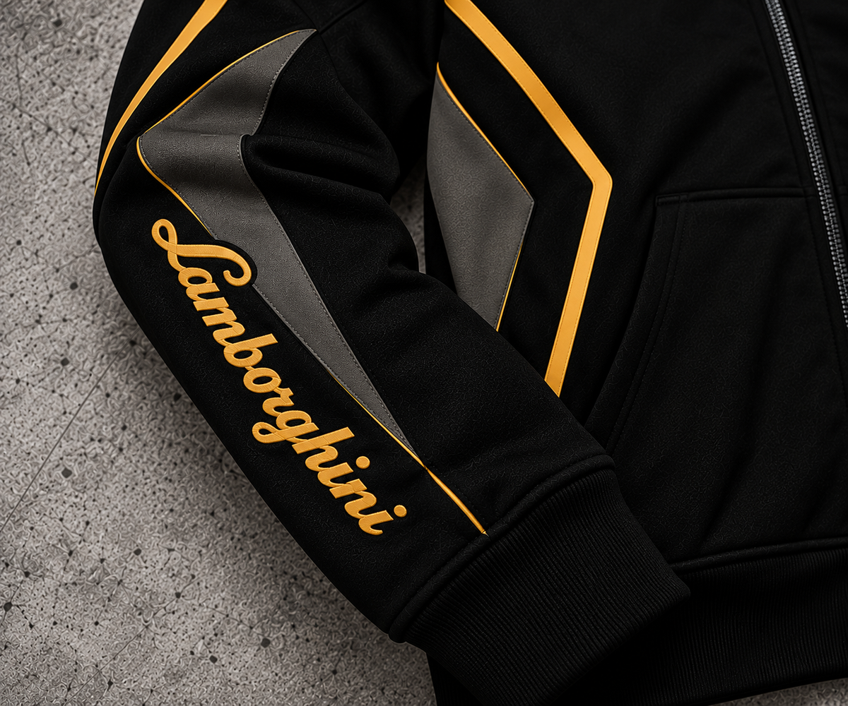 REVLINE Lamborghini hoodie sleeve close-up gold Lamborghini script, gold piping, charcoal panels on grey concrete