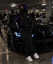 BMW design hoodie female lifestyle realistic underground car meet with integrated balaclava beside black BMW M4 Competition