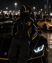 REVLINE Lamborghini hoodie male lifestyle nighttime car meet, black and gold balaclava hoodie, gold shield chest and Lamborghini script sleeve